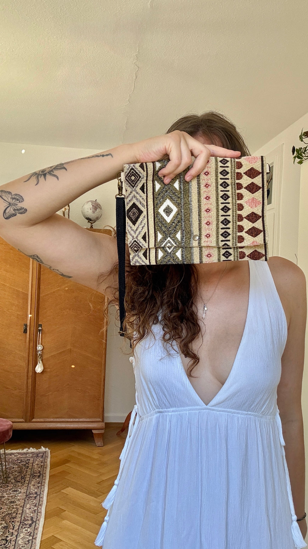 Frau im weißen Kleid mit Boho Tasche vor dem Gesicht