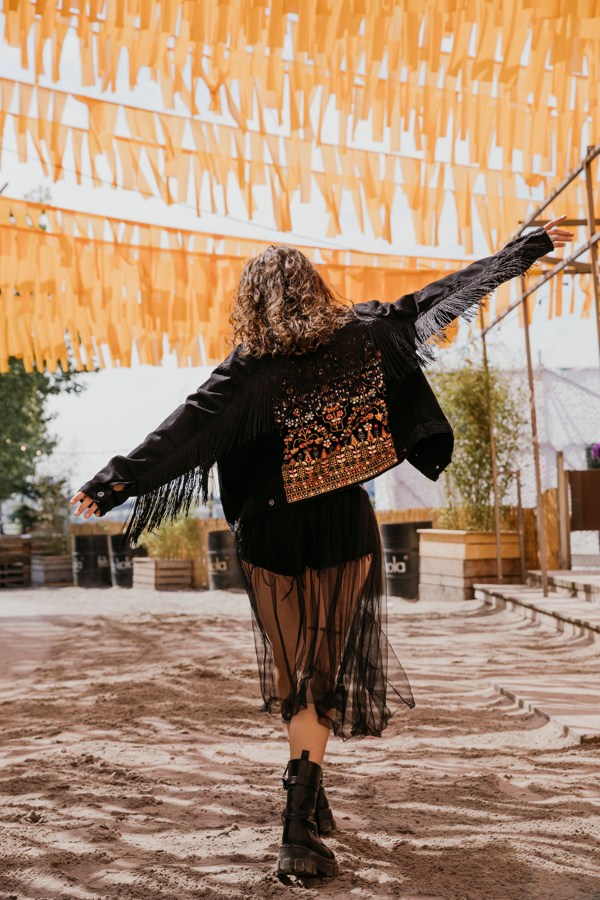 Bild von einem Mädchen auf einem Festival-Gelände in einer Hippie Jacke ihr Festivaloutfit